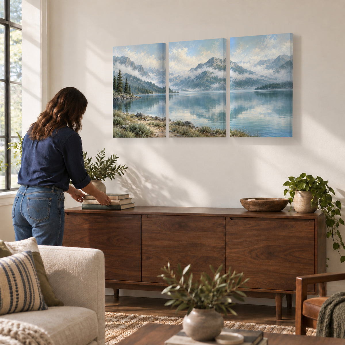 Misty Mountain Lake triptych canvas prints above a sideboard while arranging books